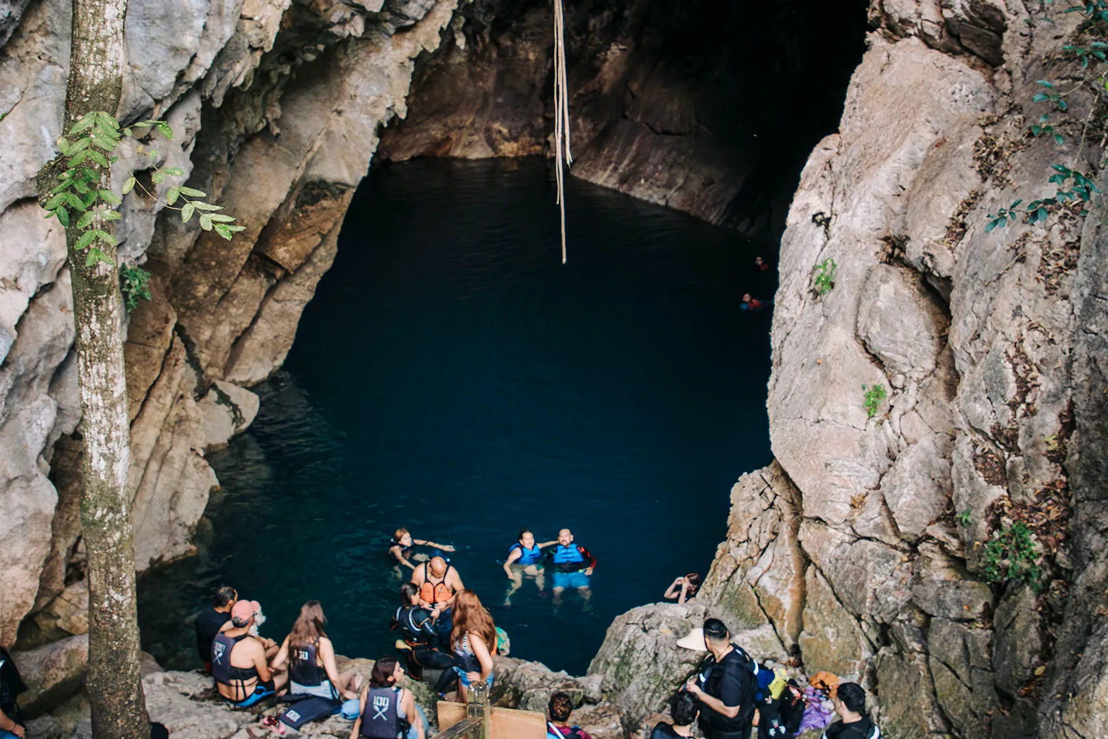 Grupo de turistas y buceadores preparándose para nadar en una fosa natural de aguas profundas rodeada de formaciones rocosas en Rioverde, San Luis Potosí.