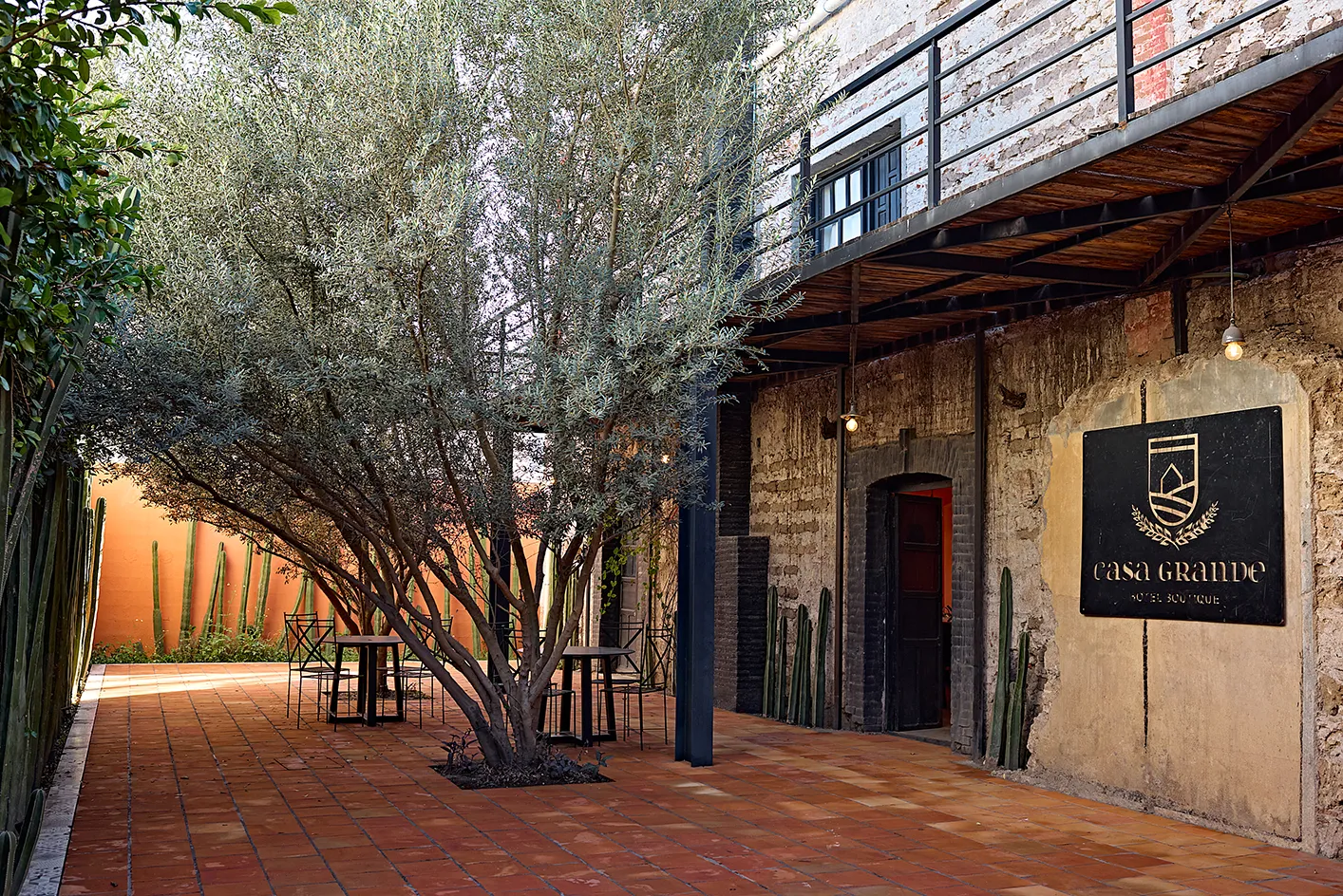 Entrada principal de Casa Grande Hotel Boutique en Rioverde, San Luis Potosí, con letrero metálico sobre muro rústico, patio de terracota y olivo central.