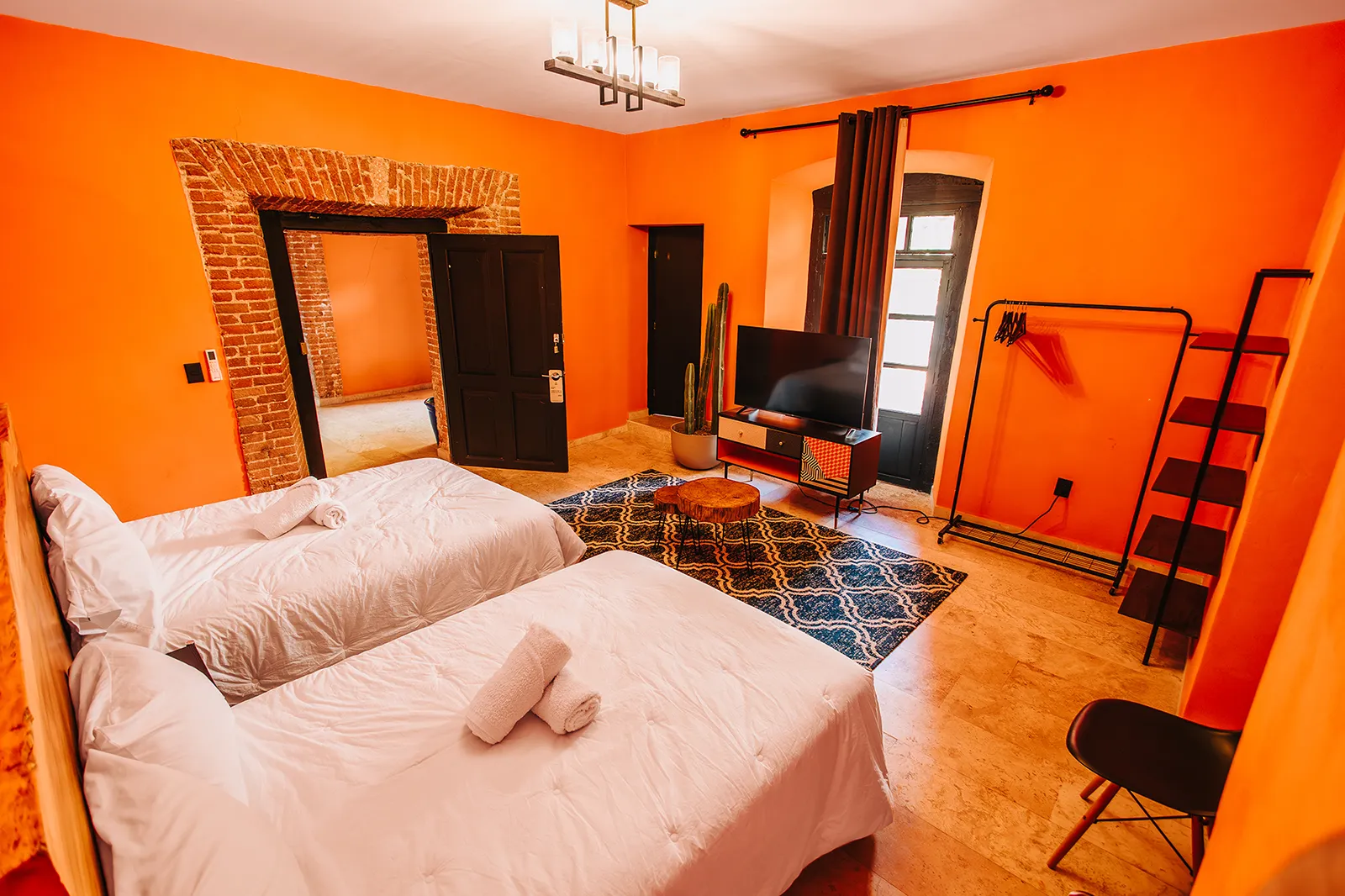 Habitación de hotel en Rioverde SLP con paredes naranja, dos camas matrimoniales, detalles de ladrillo rústico y decoración mexicana contemporánea.