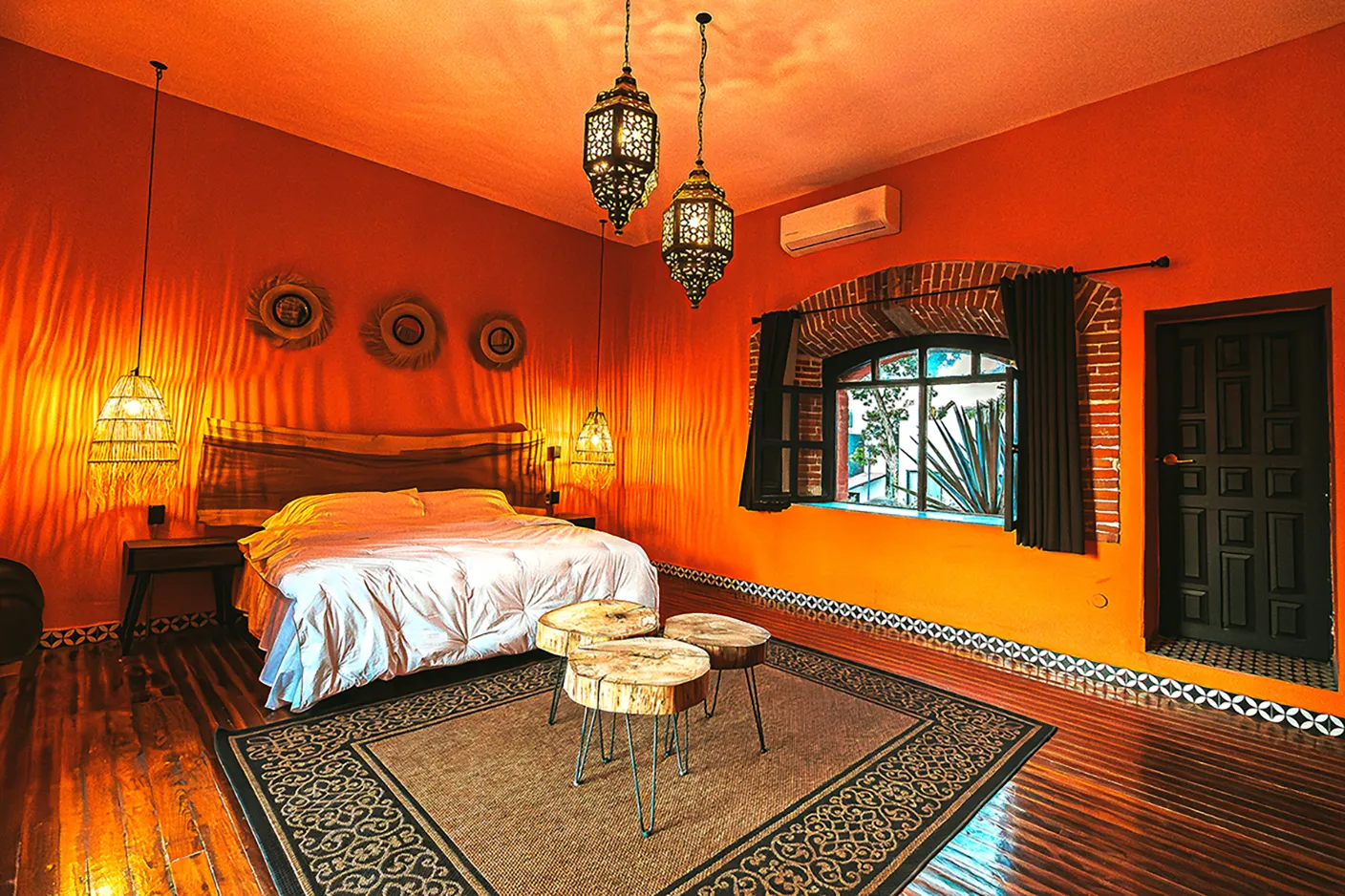 Habitación de lujo en Casa Grande Río - Hotel Boutique con muros color naranja, cama king size, lámparas colgantes de estilo árabe, ventanal de ladrillo y decoración rústica moderna en Rioverde.