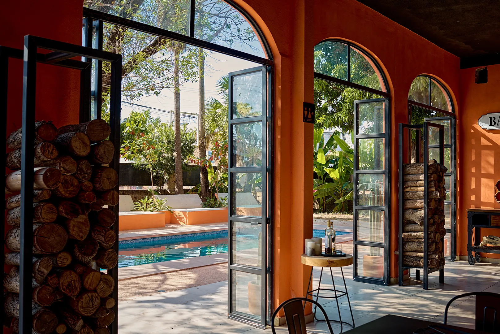Interior de hotel boutique con arcos de medio punto, ventanales industriales y estantes con leña, con vista hacia la alberca y jardines en Rioverde, San Luis Potosí.